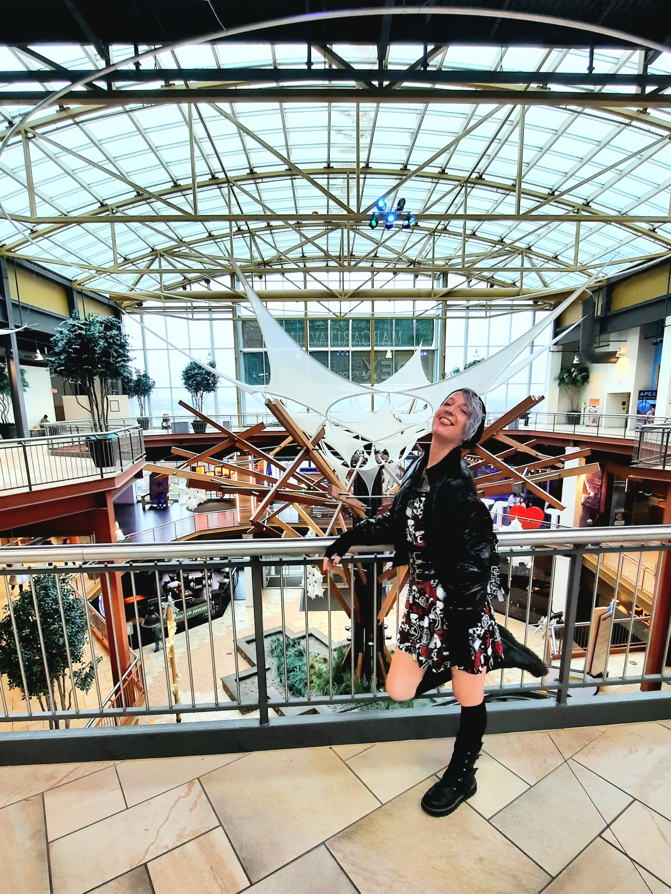 Kae Audhild at Destiny USA mall in Syracuse, NY, Central New York attractions, alternative goth punk lifestyle fashion beauty travel blogger, keracolor silver blue toning semipermanent hair toning color conditioner, killstar x rob zombie official print bardeau style goth punk skater dress, shein black faux leather studded buckle corset style waist belt, shein sxy shiny black puffer bomber jacket, black knee high socks from Amazon, black vegan leather Demonia Lilith-211 mid-calf buckle side zip boots, best of winter 2023 goth fashion, tattooed pierced alt models, thick coarse curly bleached icy blue hair, real natural scandi curls waves, women's afab nonbinary asymmetrical undercut hairstyles