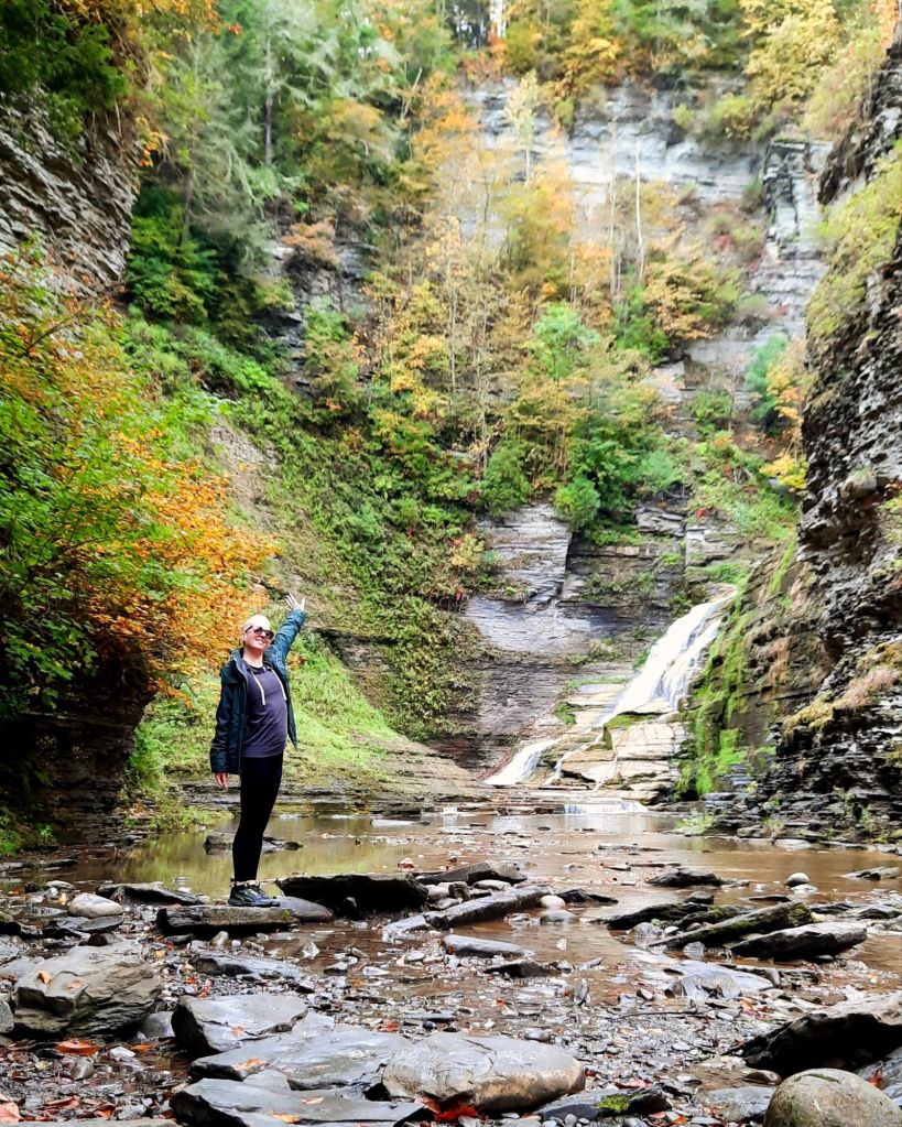 Kae Audhild standing at the base of Lucifer Falls at Robert H Treman State Park in Ithaca ny October 2024 autumn foliage fall hiking Finger Lakes flx outdoors recreation fitness