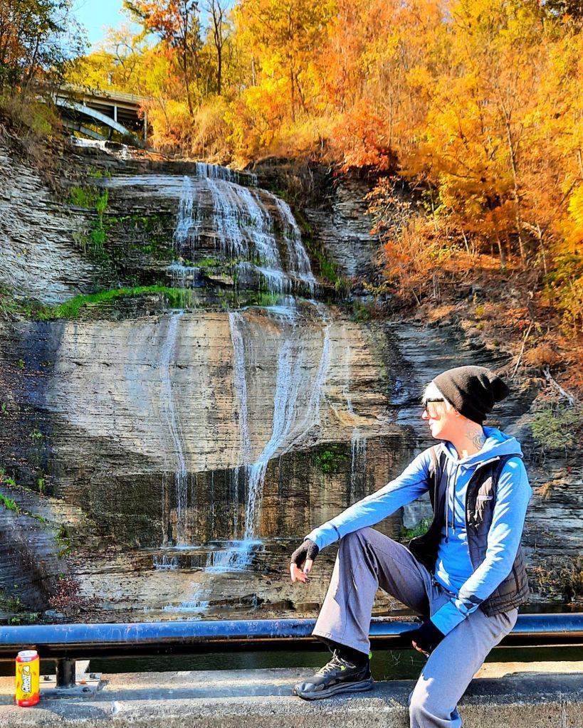 Kae Audhild sitting at Chequaga Shequaga Falls waterfall in Montour Falls, New York, Finger Lakes region, cny flx autumn foliage, travel blog