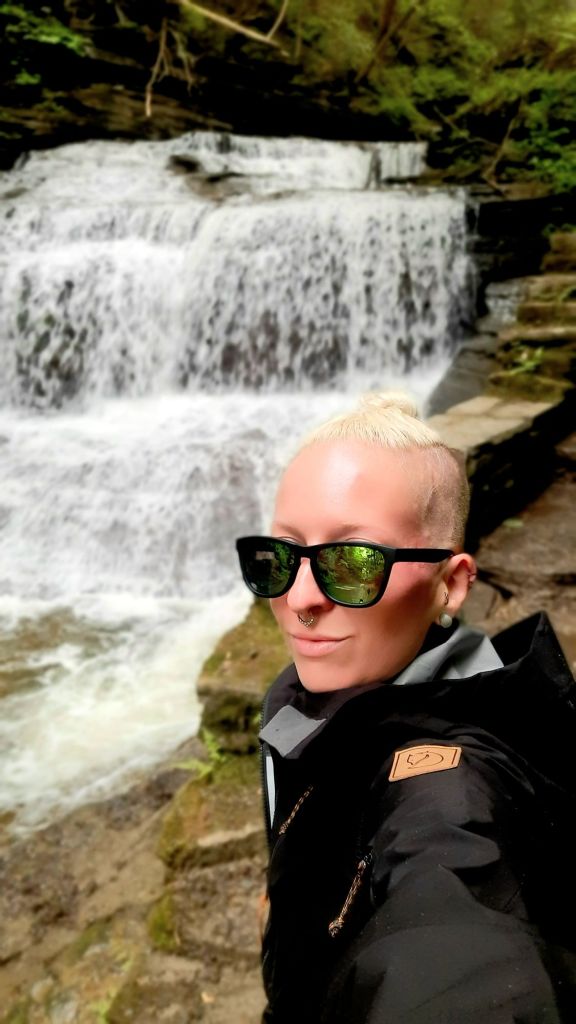 Kae Audhild hiking selfie in front of a waterfall along the gorge trail at Buttermilk Falls State Park in Ithaca, NY - travel outdoor fitness lifestyle blogger