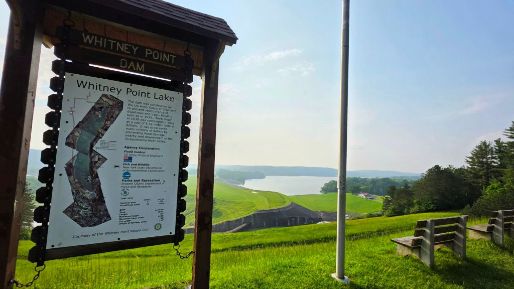 View of the Whitney Point Lake + Dam overlook, info sign and benches in the foreground