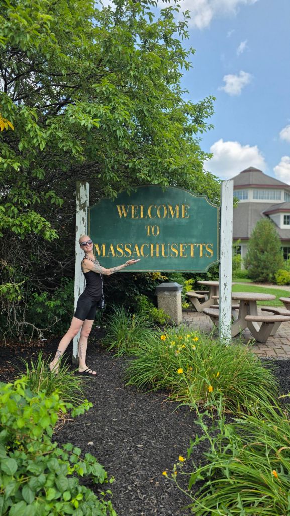 Kae Audhild with welcome to Massachusetts sign at pit stop after crossing the state border from New York