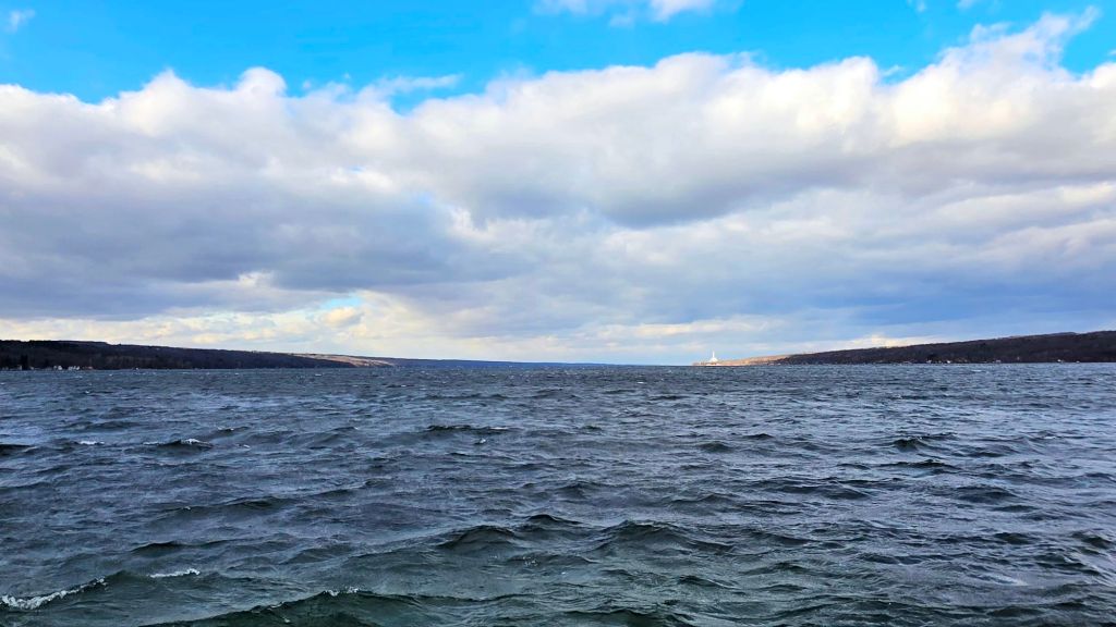 Windy winter view of Cayuga Lake from Taughannock Point, with choppy water, dramatic clouds, and distant shoreline in the Finger Lakes of Upstate New York.