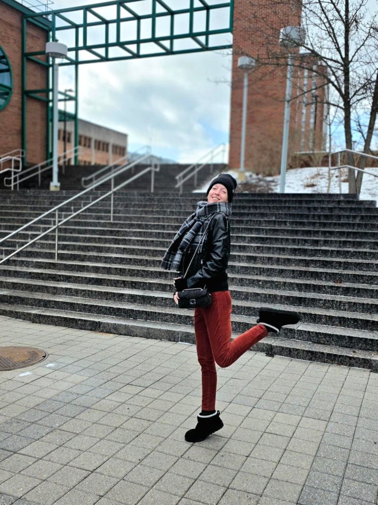 Winter on-the-go outfit featuring a black Carhartt beanie, Michael Kors grey plaid scarf, black leather jacket, burnt orange corduroy pants from Banana Republic, Coach Tabby 20 grey denim bag, and black UGG Classic Ultra Mini Maxi Curly boots, styled for a casual city walk.