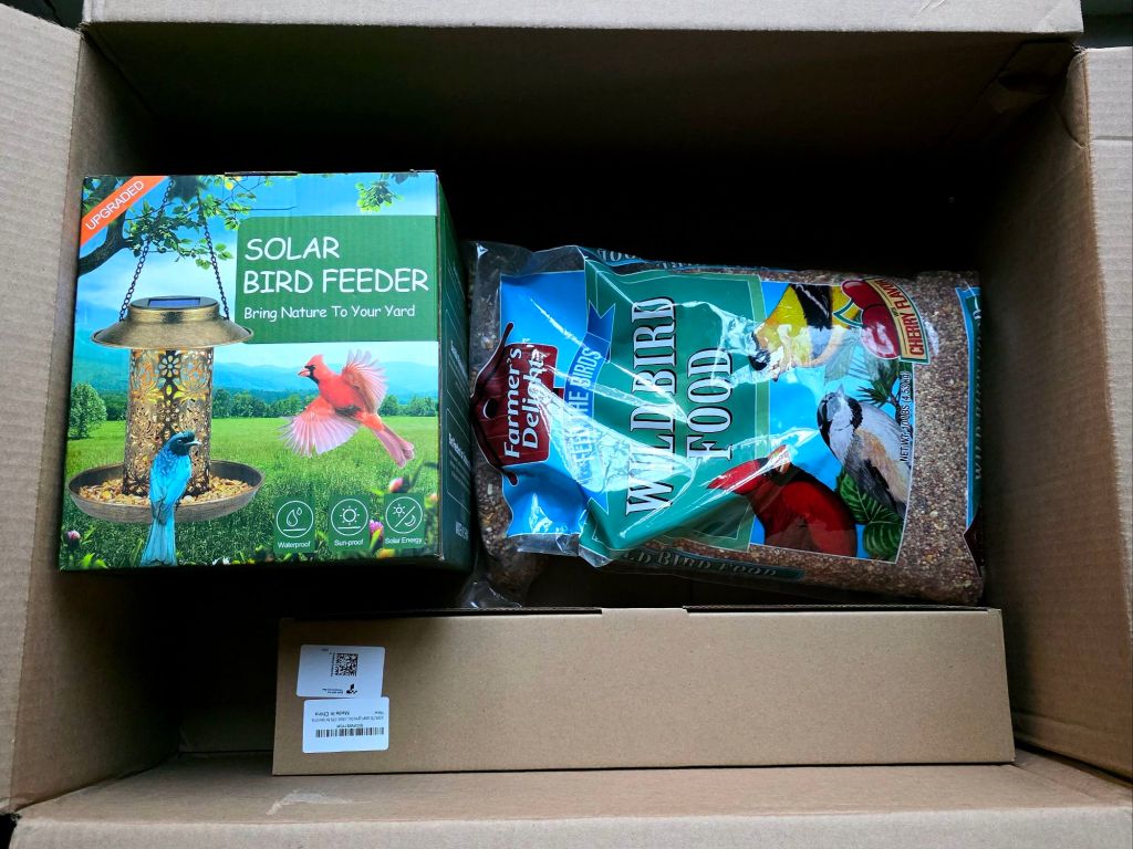 Amazon order showing a solar hanging metal bird feeder and a bag of wild bird food inside an open cardboard shipping box