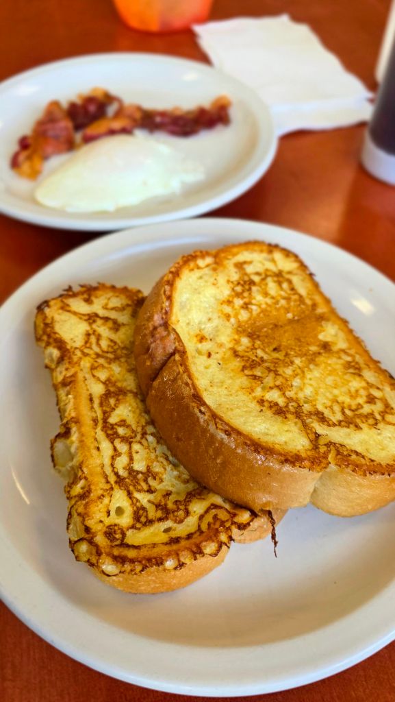 Plate of French toast with bacon and a medium-cooked egg at Piccolo’s Cafe in Binghamton, New York, served on a white diner plate during a cozy breakfast.