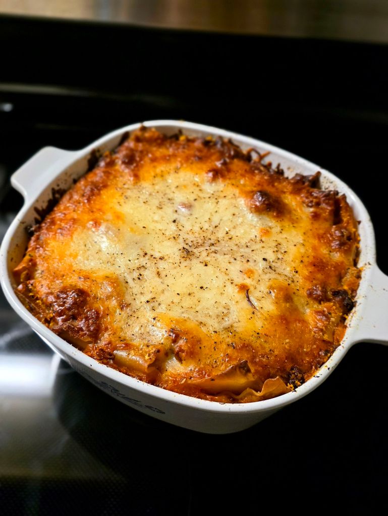 Baked flavor-forward lasagna in a vintage blue cornflower CorningWare casserole dish with melted cheese and black pepper, fresh from the oven.