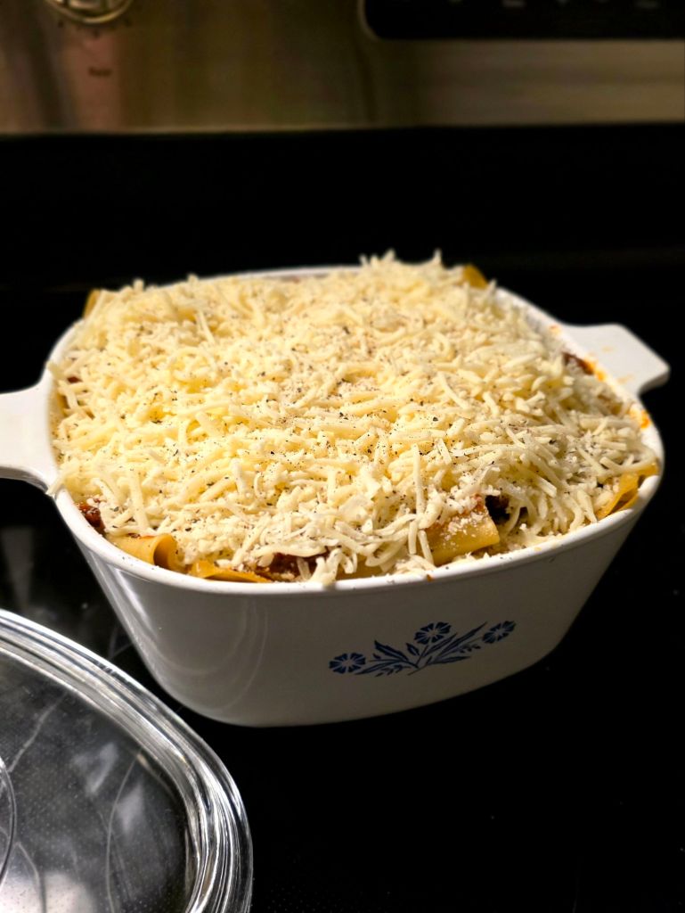Unbaked homemade lasagna layered with meat sauce, ricotta, and shredded mozzarella in a vintage blue cornflower CorningWare casserole dish before baking.